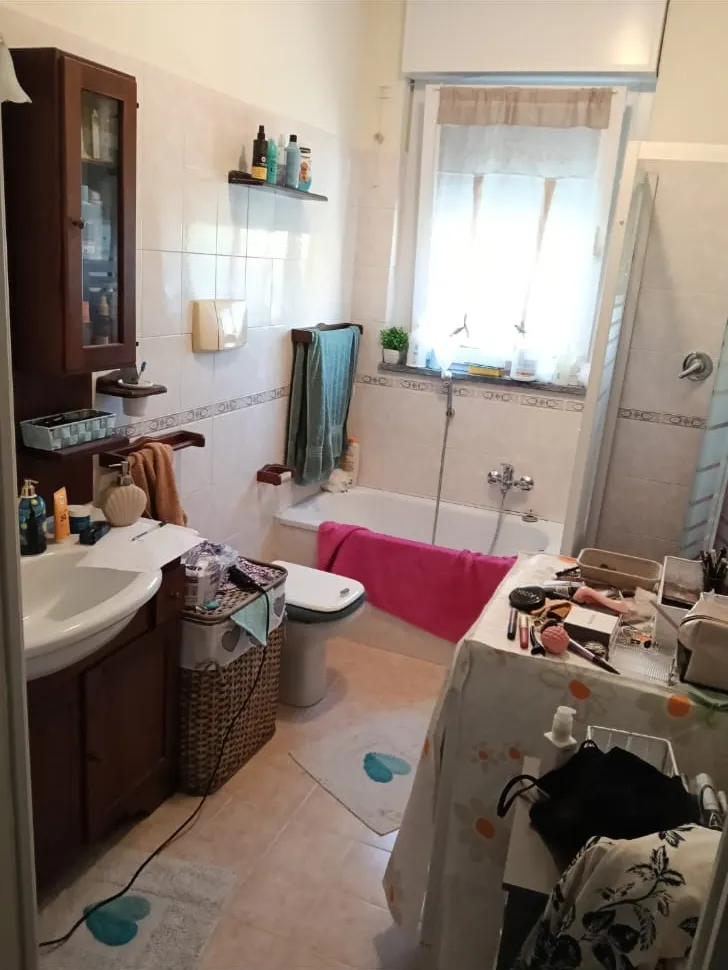 Un bagno prima dell'intervento: piastrelle chiare, vasca e mobili in legno scuro
