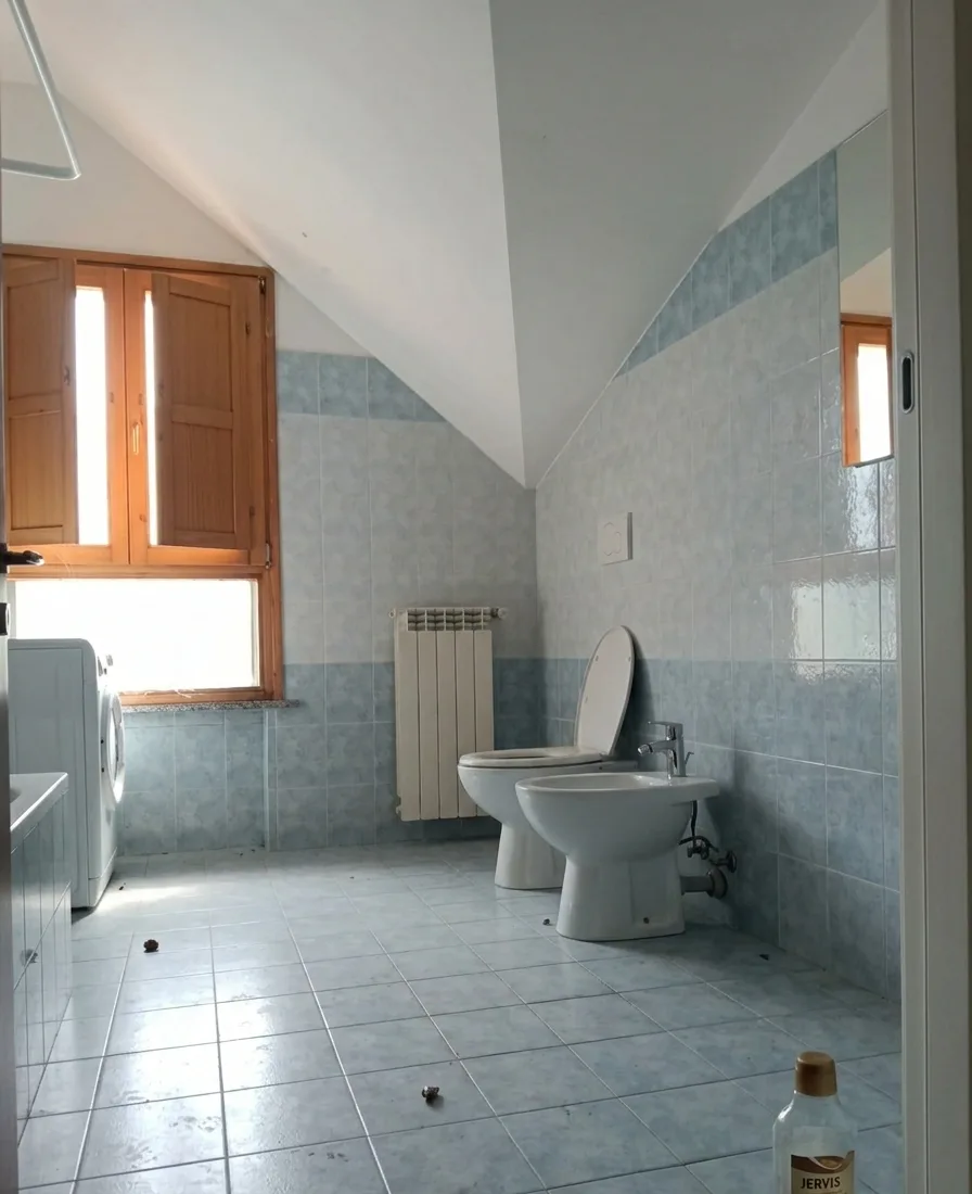 Bagno mansardato con piastrelle azzurre e pavimento in ceramica, prima dell'intervento